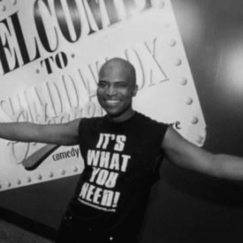 A man standing in front of a sign that says "Welcome to Shadowbox," showcasing the rich history.