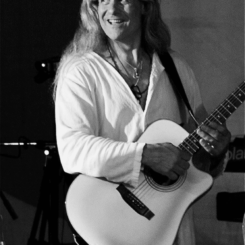 A man with long hair playing an acoustic guitar.