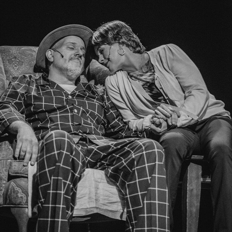 A man and woman in pajamas sitting on a chair, giving each other affectionate ways.