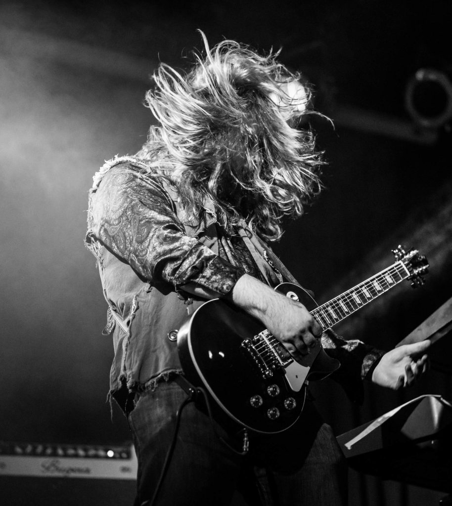 A man with long hair playing a guitar on stage.