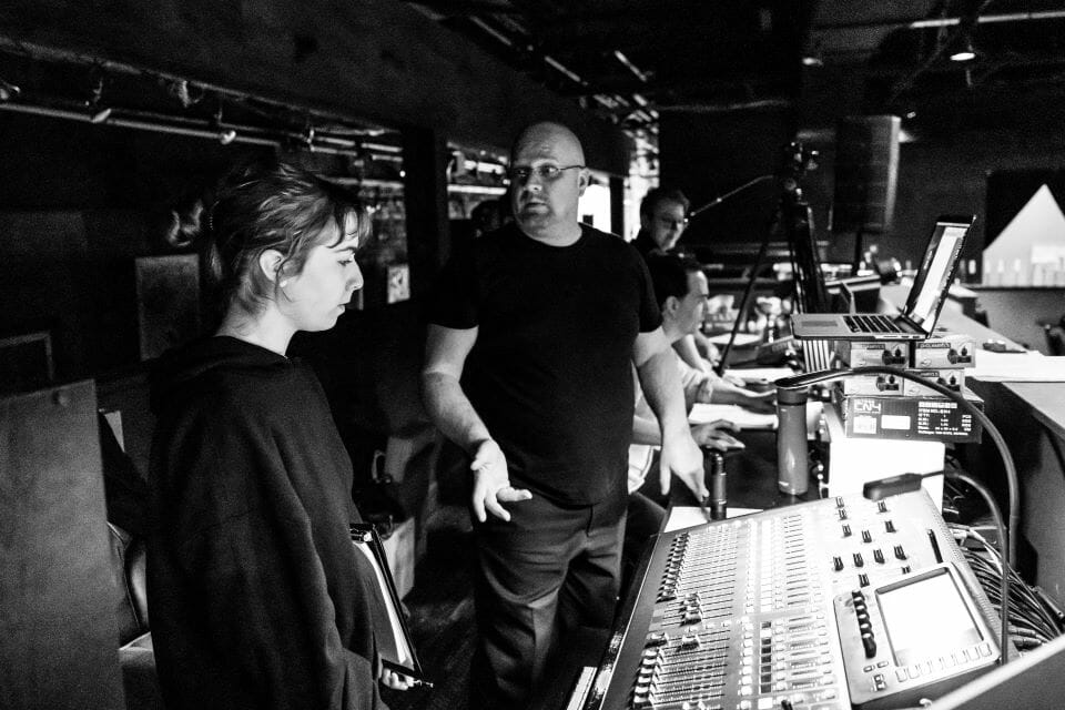 Two people standing in front of a mixing board.